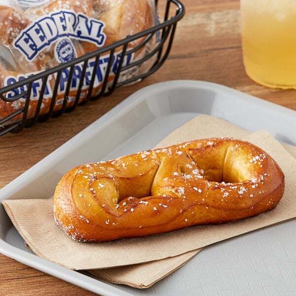 An individually wrapped soft pretzel on a tray next to a yellow liquid.