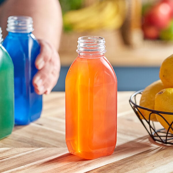 A hand holding a blue 12 oz. Square Milkman PET clear juice bottle next to a bowl of fruit.