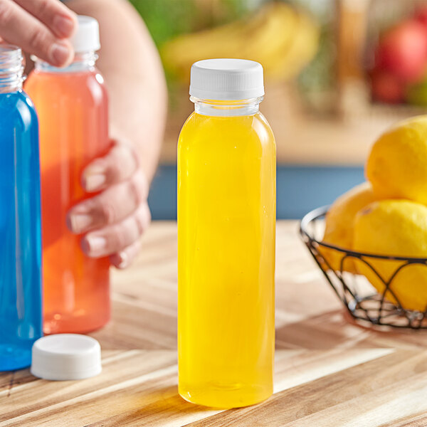 A person's hand holding yellow and orange 12 oz. PET juice bottles with white caps.