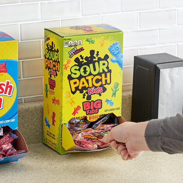A hand reaching into a black box of Sour Patch Kids with different colored characters.