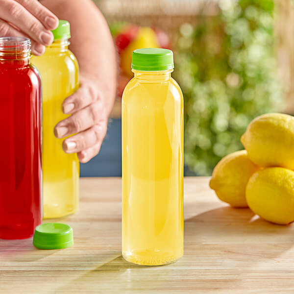 A person holding a 16 oz. round clear juice bottle with a yellow liquid and a lime green lid.