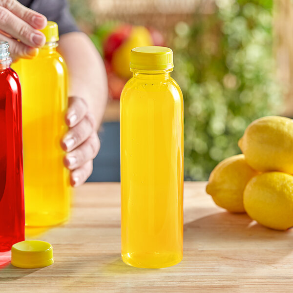 A person holding a 16 oz. round clear PET juice bottle with a yellow lid filled with yellow liquid.