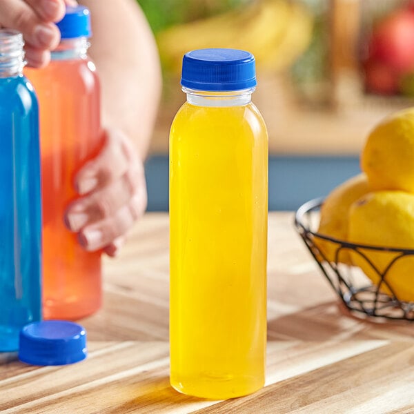 A person holding a 12 oz. round PET clear juice bottle with yellow liquid and a blue cap.