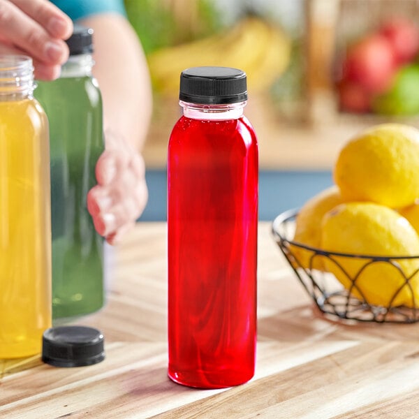 A person pouring red juice into a 12 oz. clear round PET juice bottle with a black lid.