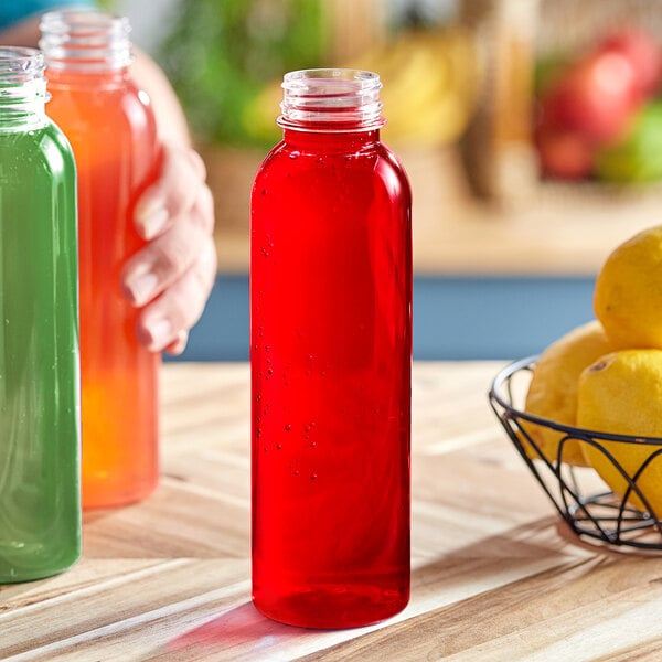 A hand holding a red liquid-filled 16 oz. Round PET Clear HPP Juice Bottle next to a bowl of lemons.