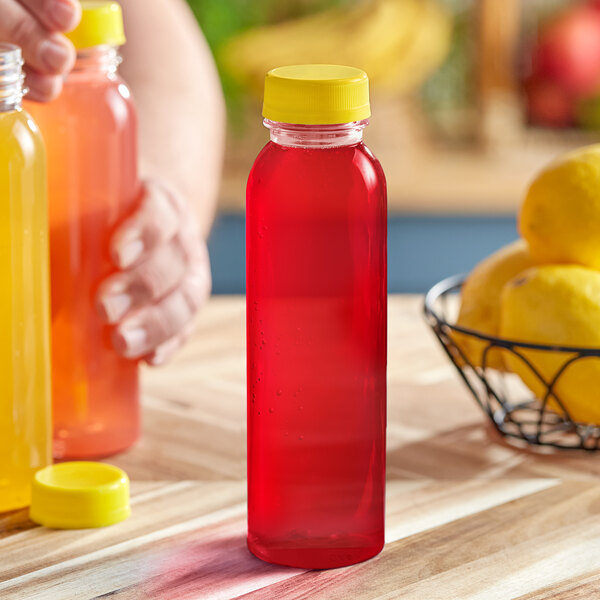 A hand holding a 12 oz. round clear PET juice bottle with yellow and orange liquid inside and a yellow lid.