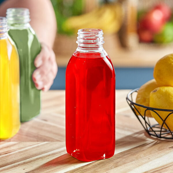 A person holding a 16 oz. Square Milkman PET clear juice bottle full of red liquid next to a bowl of yellow lemons.