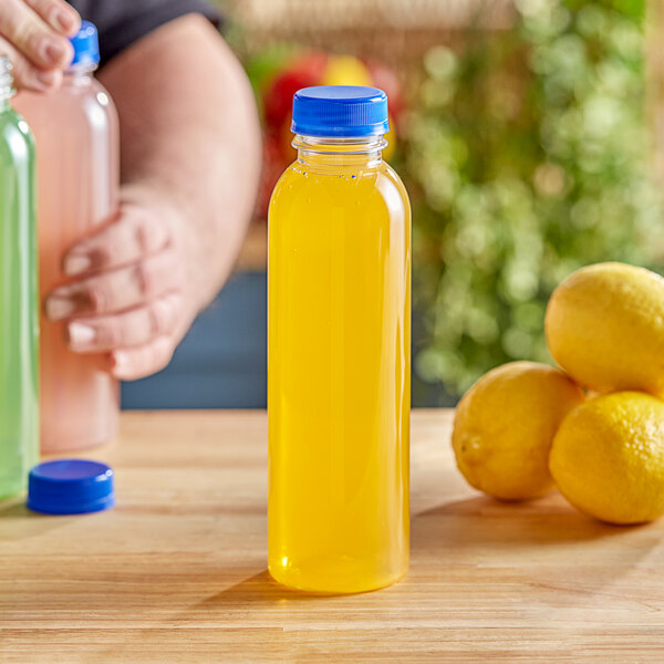 A hand holding a 16 oz. round PET clear juice bottle with yellow liquid.