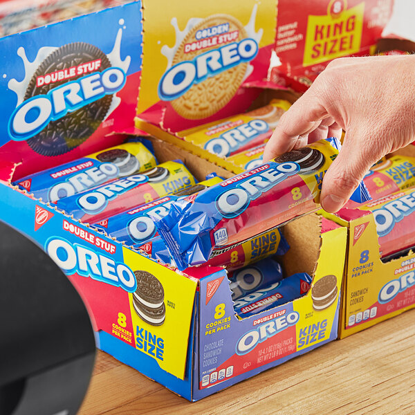 A hand holding a box of Nabisco Oreo King Size Double Stuf cookie snack packs.