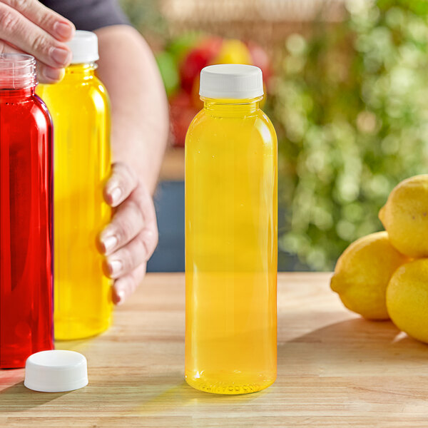 A person pouring lemon juice into a yellow 16 oz. round PET juice bottle with a white lid.