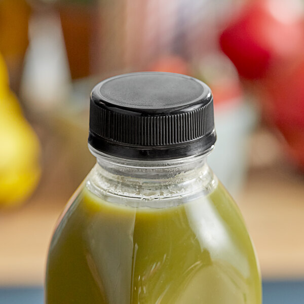 A black tamper-evident cap on a bottle of green juice.