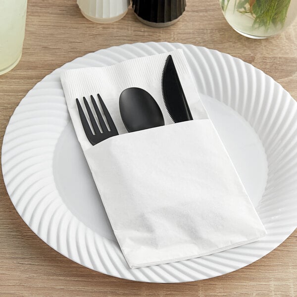 A white paper plate with a Hoffmaster Quickset white pocket fold dinner napkin with a black spoon and fork.