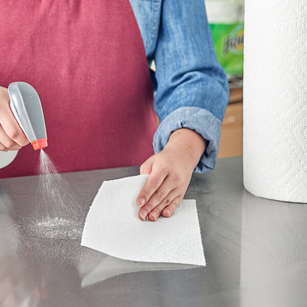 A person using a sprayer to spray a Bounty paper towel on a counter.