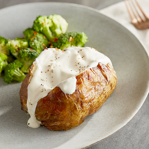 A plate with a baked potato topped with white sauce and broccoli with a fork.