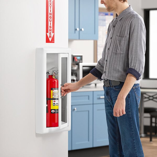 A man opening a white steel cabinet to reveal a Badger fire extinguisher inside.