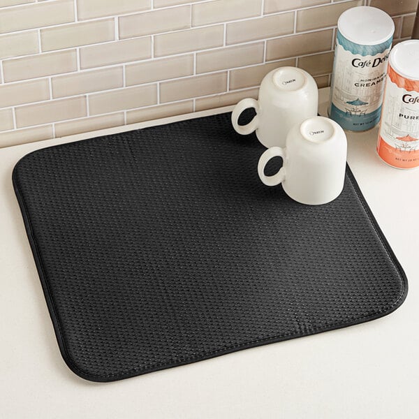 A black Envision Home dish mat with two white mugs on it.