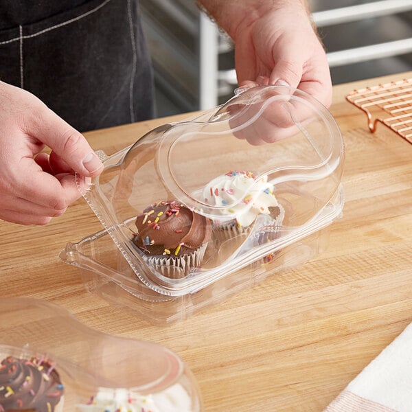 A person opening a InnoPak plastic container of cupcakes with a clear dome lid.