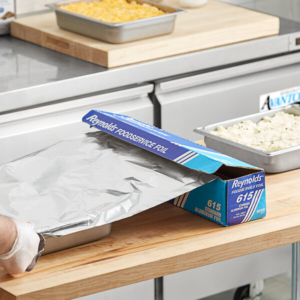 A person using Reynolds aluminum foil to cover food in a pan.