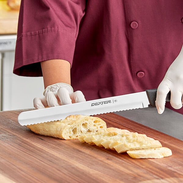 A person in a chef's uniform using a Dexter-Russell scalloped bread knife to slice bread.