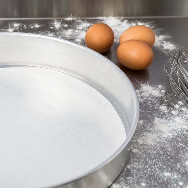 A metal pan lined with Baker's Lane parchment paper with a bowl of brown eggs and flour.