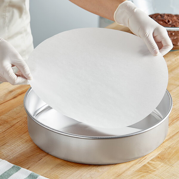 A person in white gloves using a Baker's Lane round white silicone coated pan liner to make a cake.