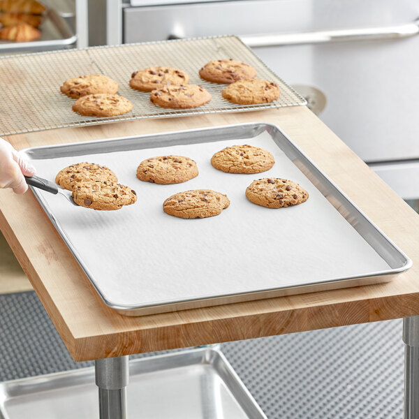 A person using a Baker's Lane parchment paper sheet to line a cookie sheet on a table.