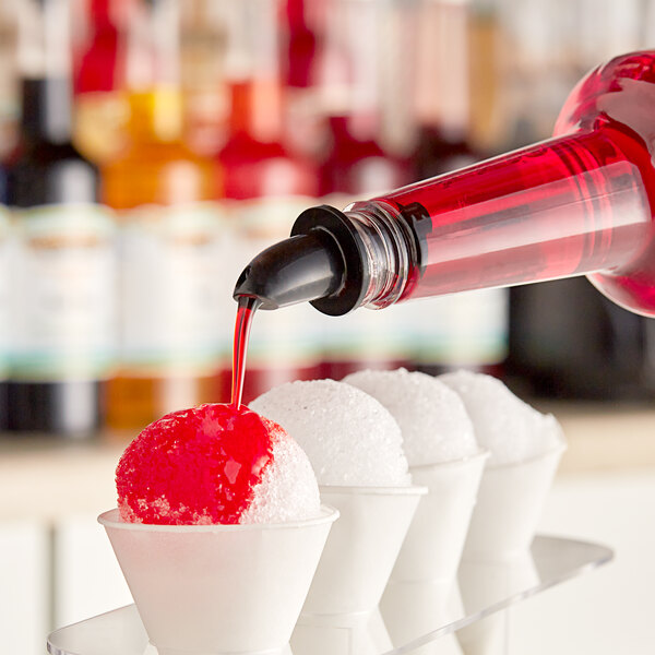 A person pouring Hawaiian Shaved Ice Cherry Snow Cone Syrup into a white cup.