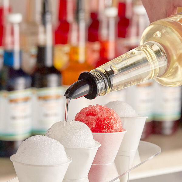 A person pouring Hawaiian Shaved Ice Coconut syrup on a bowl of snow cones.