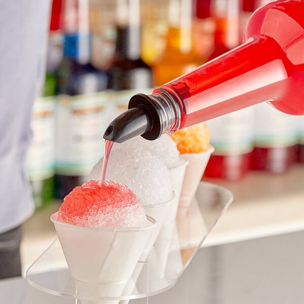 A person pouring Hawaiian Shaved Ice Pink Bubble Gum syrup into a cup of ice.