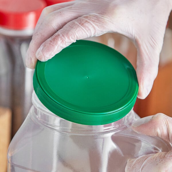 A gloved hand holds a 110/400 green flat top lid over a container.