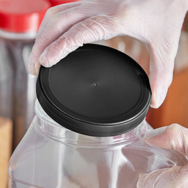 A person in gloves holding a 110/400 black flat top induction-lined lid.