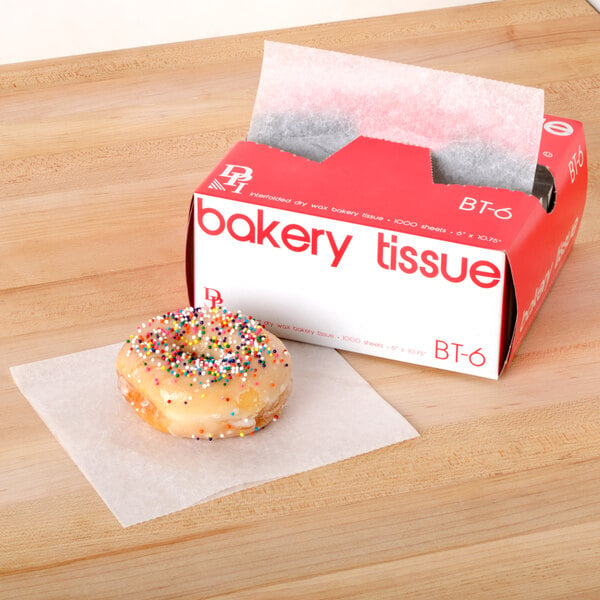 A donut with sprinkles on top of it next to a box of Durable Packaging bakery tissue.