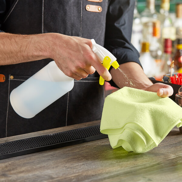 A person using a Lavex yellow spray bottle to clean a bar counter.