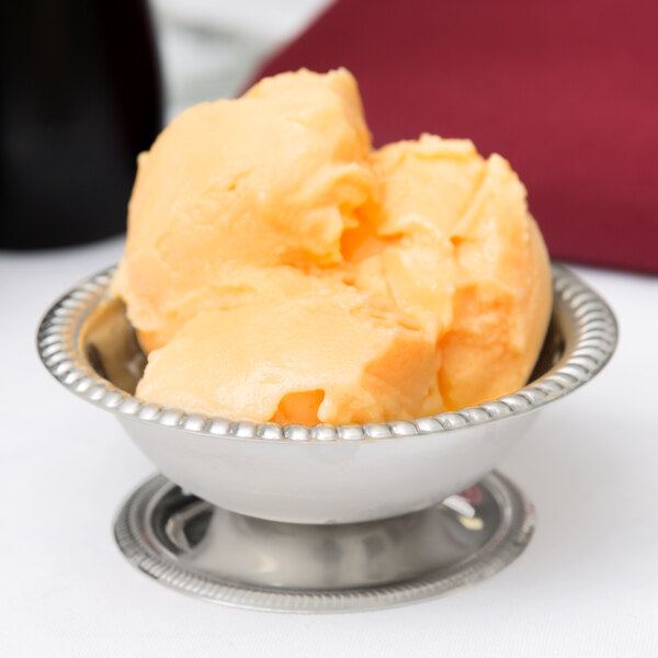 A stainless steel Vollrath sherbet dish filled with orange ice cream.