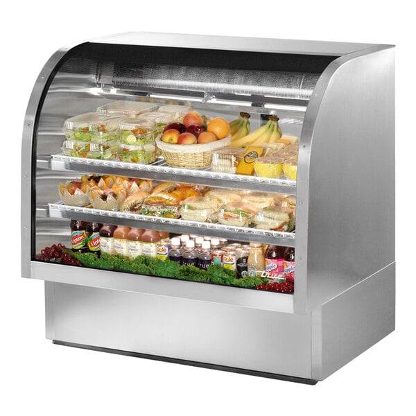 A True stainless steel curved glass refrigerated deli case with food displayed inside.