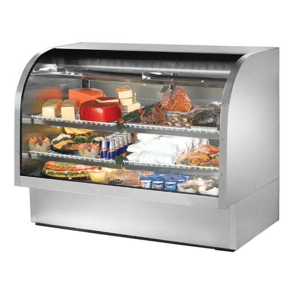 A True stainless steel curved glass deli case full of food on shelves.