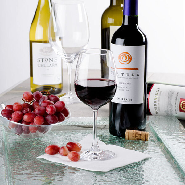 A table with a Stolzle Weinland white wine glass filled with red wine next to grapes and a bottle of wine.