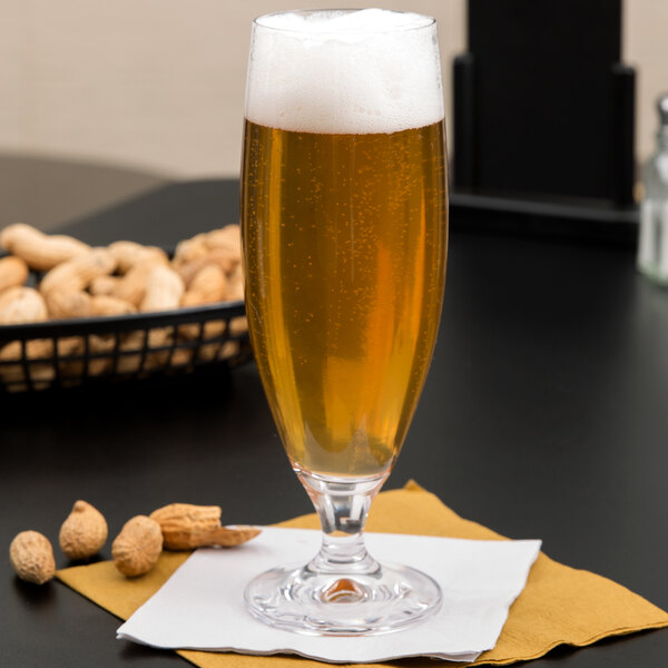 A Stolzle Imperial stemmed beer glass full of beer on a napkin next to a basket of peanuts.