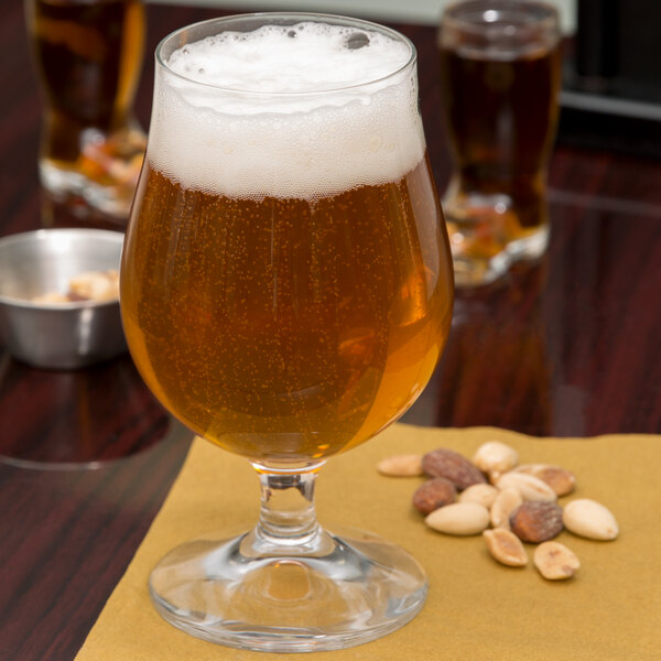 A Stolzle tulip glass of beer with foam on a table with peanuts.