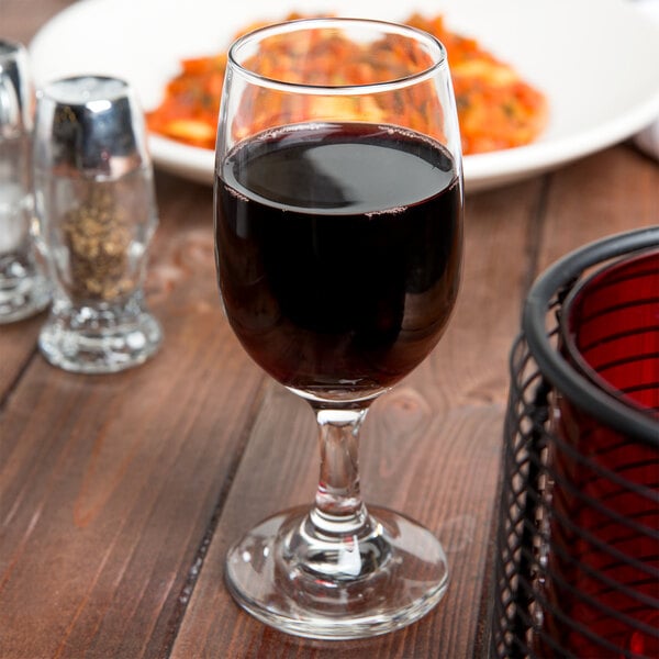 An Anchor Hocking Excellency wine glass filled with red wine on a table.