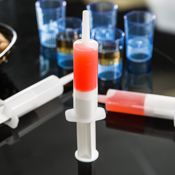 A Jell-O injector filled with red liquid sitting on a counter in a cocktail bar.