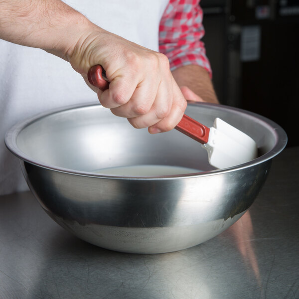 A person using a Vollrath high heat silicone spatula to mix milk in a bowl.