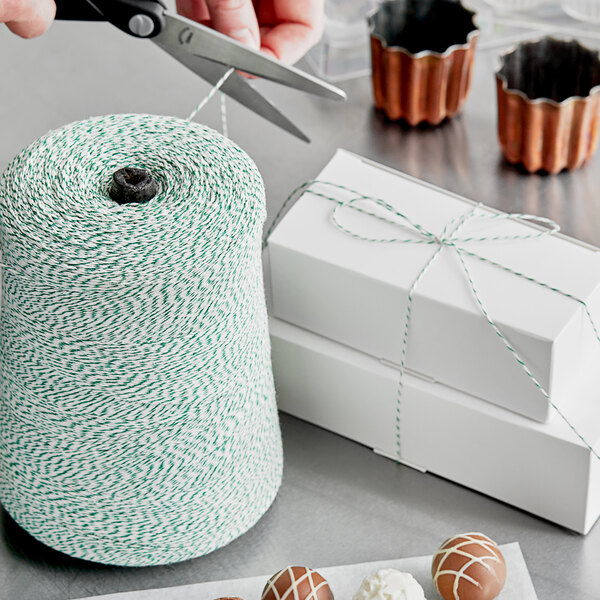 A person cutting green and white variegated Baker's Lane twine with scissors.