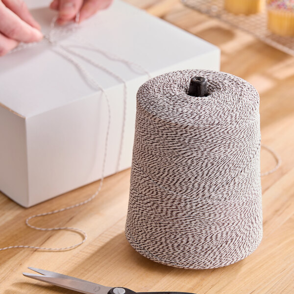 A large cone of brown and white variegated polyester cotton blend baker's twine on a wooden surface.