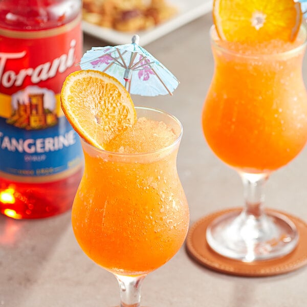 Two glasses of Torani tangerine flavored drinks with an umbrella and an orange slice.