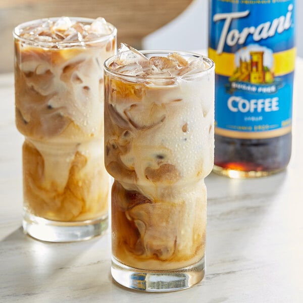 Two glasses of iced coffee and a bottle of Torani sugar-free coffee flavoring syrup.