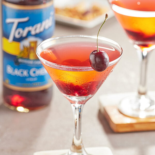 A glass of red liquid with Torani Sugar-Free Black Cherry Flavoring syrup and a cherry on top.