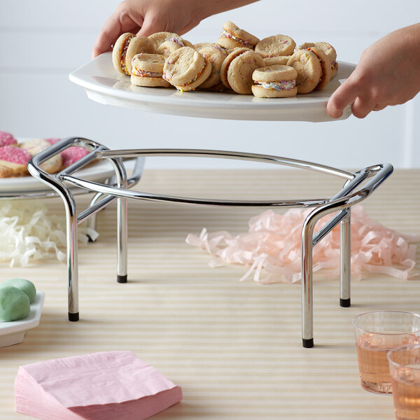 A hand holding a plate of cookies displayed on a Vollrath Display Stand.