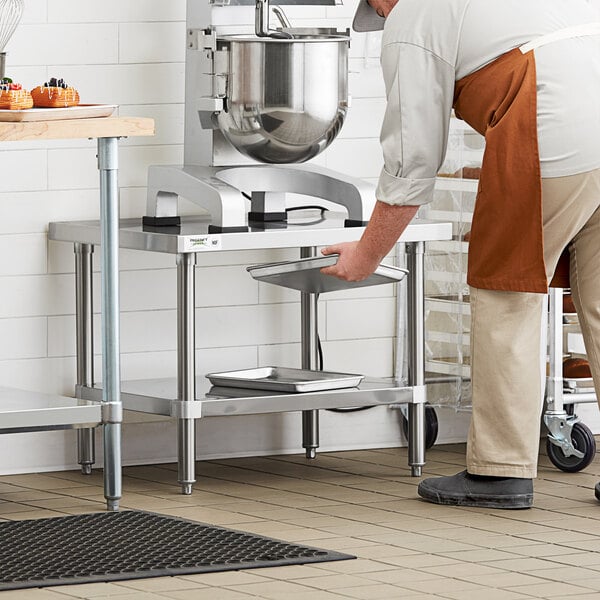 A man in an apron standing next to a Regency stainless steel mixer table with a mixer on it.