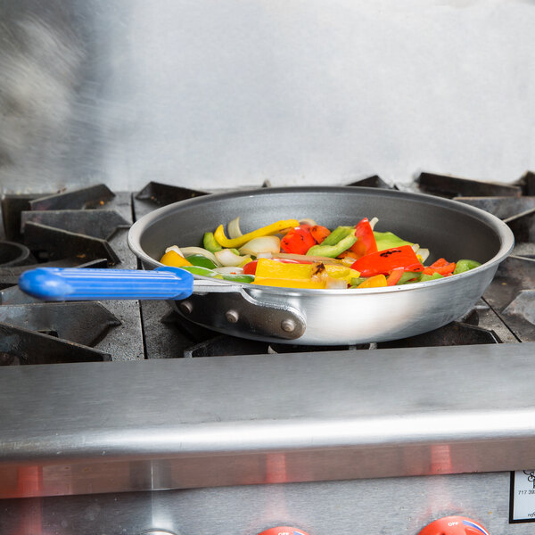 A Vollrath Wear-Ever aluminum non-stick fry pan with vegetables cooking on a stove.